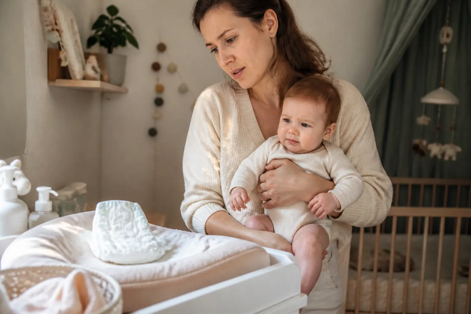 Parent inquiet tenant un bébé constipé que faire dans une chambre douce, près d’une table à langer avec couche propre.