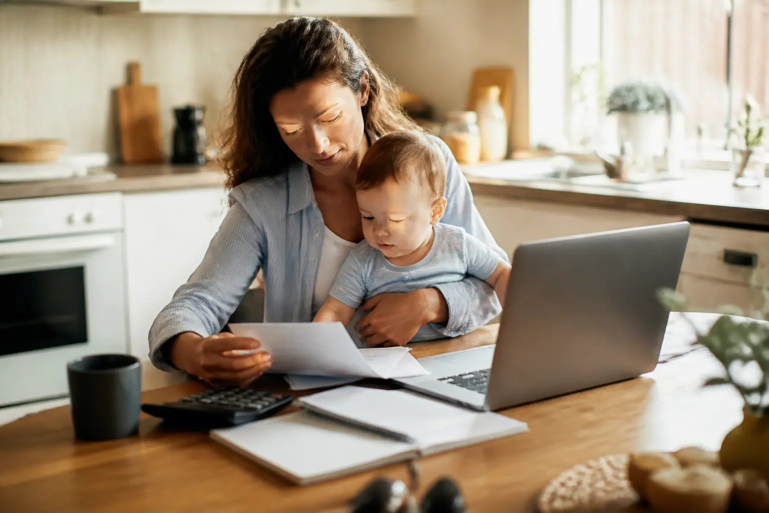 Jeune parent avec bébé, papiers et ordinateur à la maison, illustrant le congé parental caf et l’organisation familiale