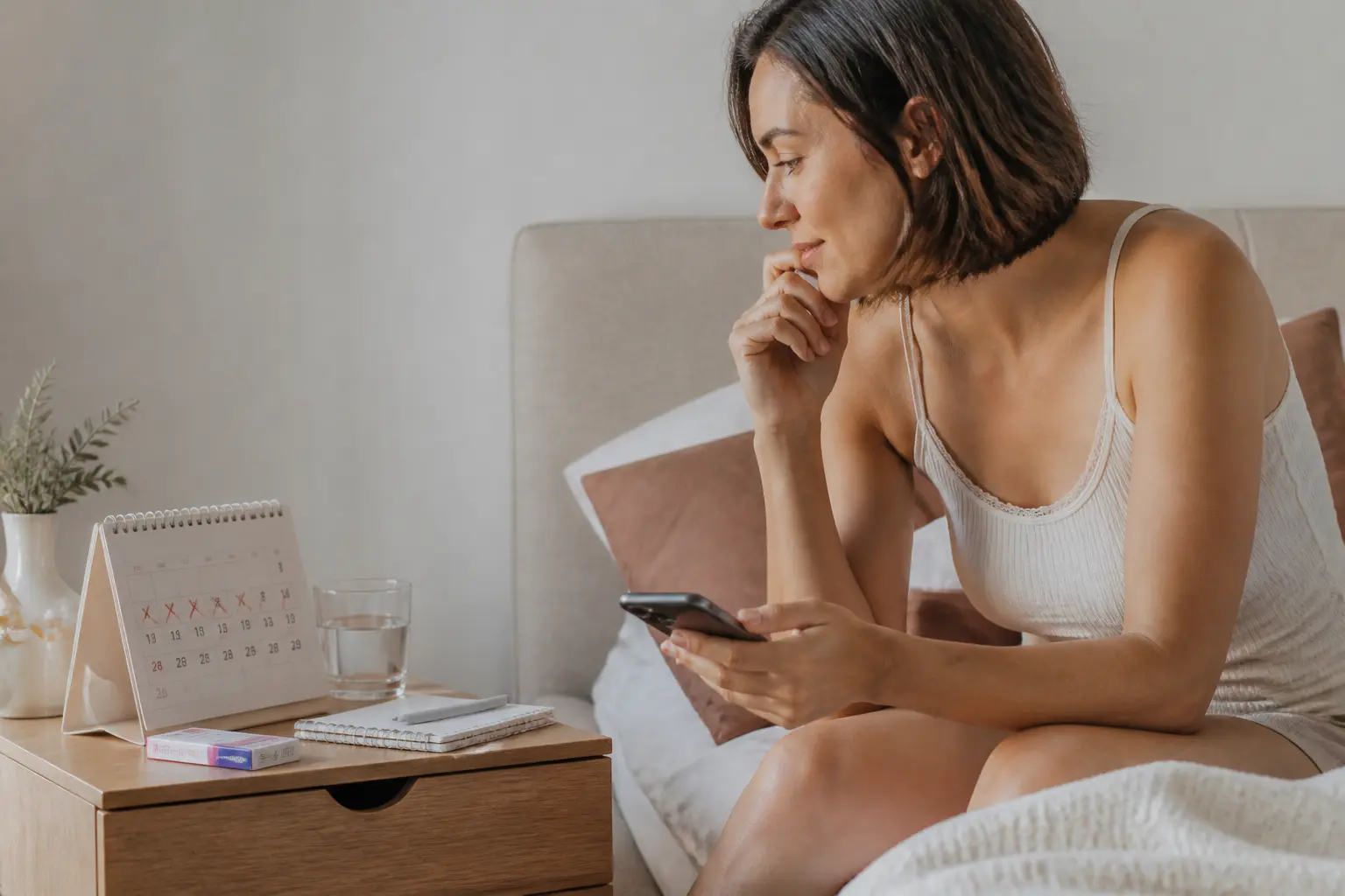 Jeune femme sur un lit, smartphone et calendrier, illustrant l'ovulation dure combien de jour dans une chambre calme.