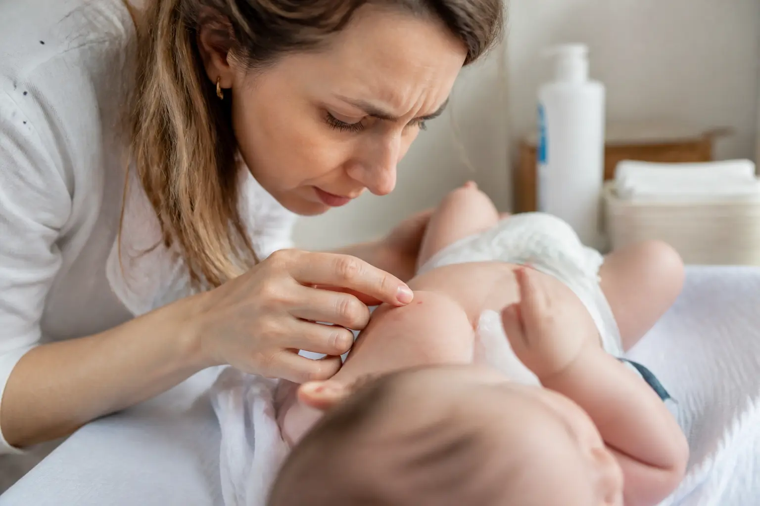 Parent examinant un petit bouton rouge bébé sans fièvre sur la peau, dans une chambre douce et rassurante