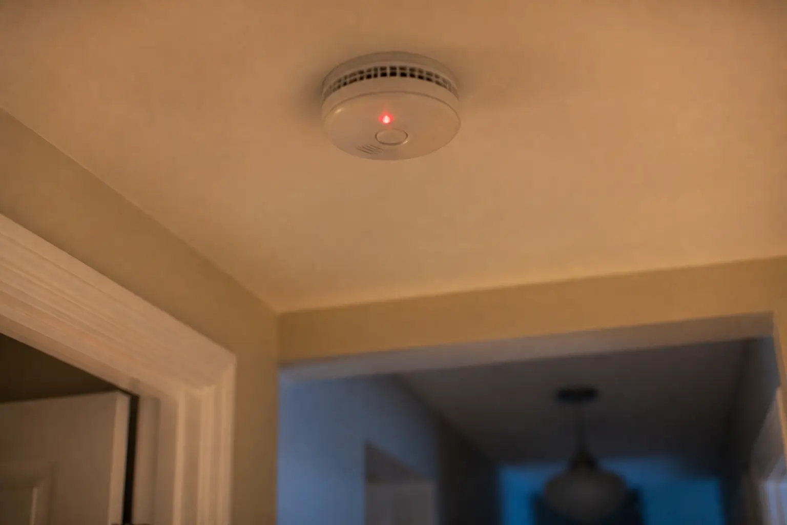 Détecteur de fumée qui bip au plafond d’un couloir sombre, vue rapprochée en intérieur, lumière chaude du soir
