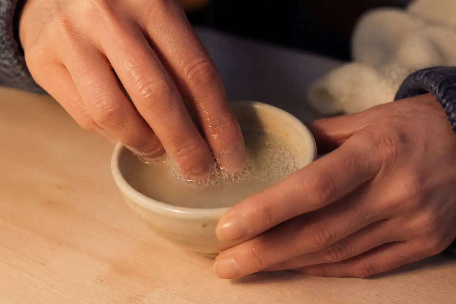 Comment enlever de la glue sur les doigts : doigts trempant dans de l’eau savonneuse tiède, glue qui ramollit sur la peau