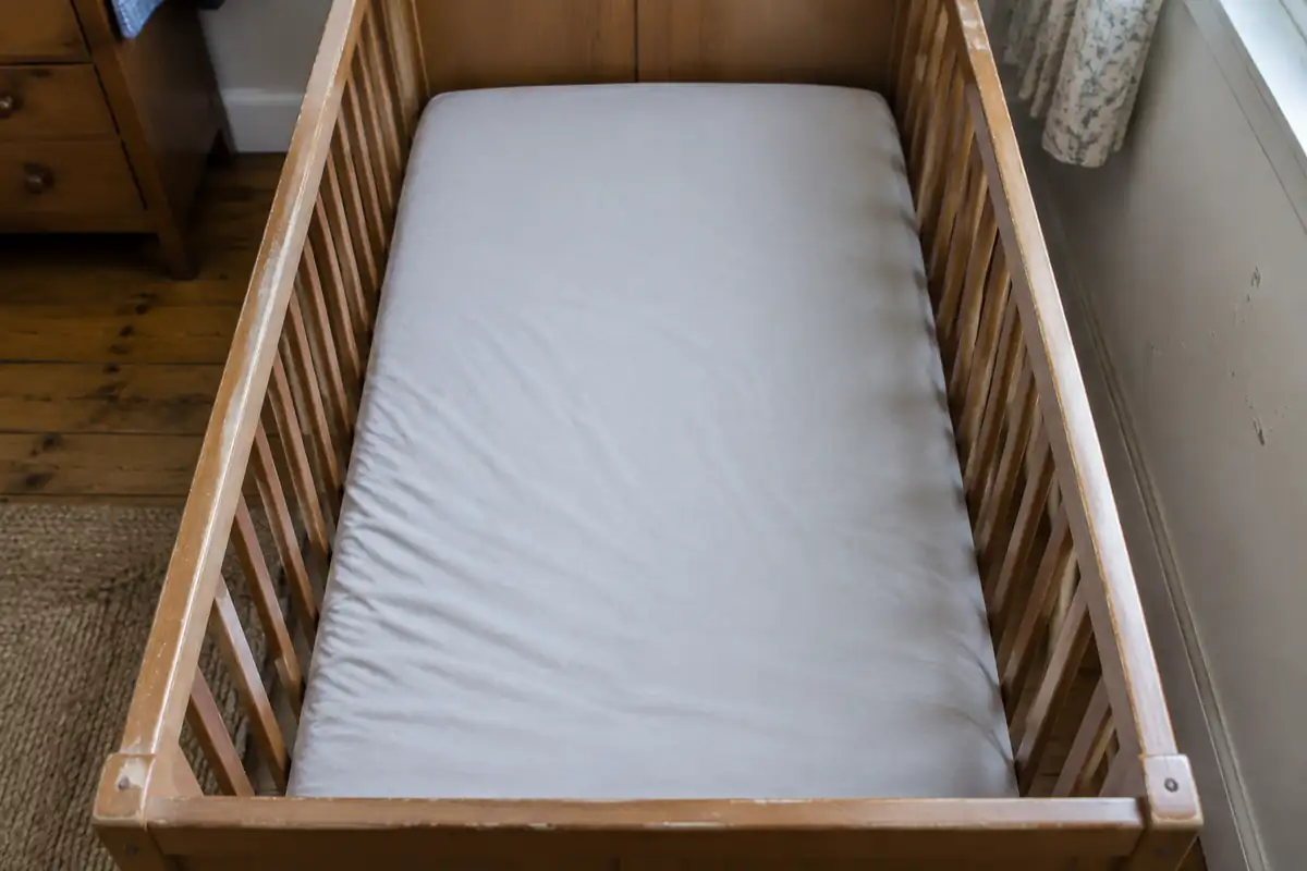 Intérieur d'un lit à barreaux avec un matelas ferme et un drap housse tendu, sans aucun objet